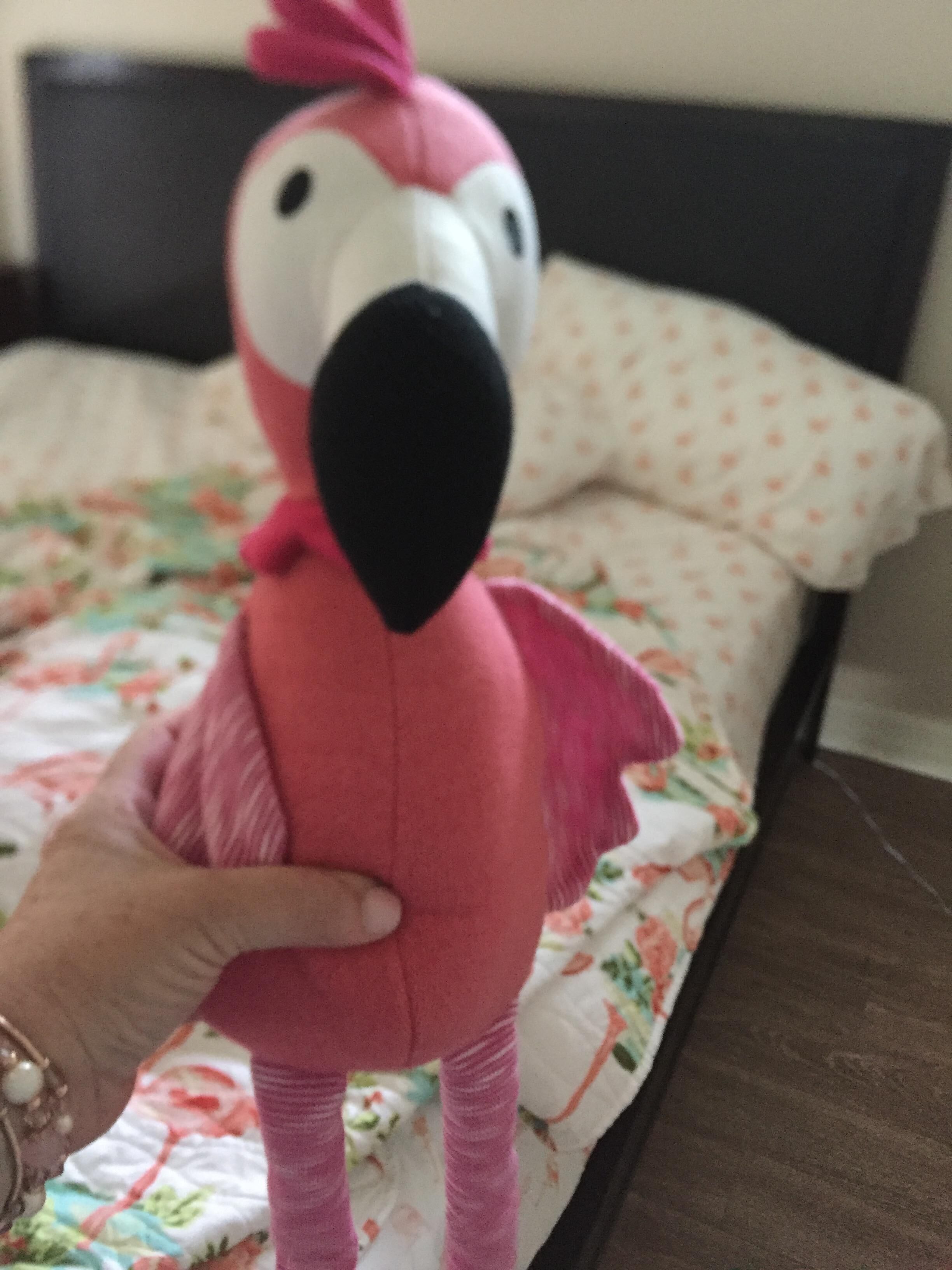 A plush toy resembling a pink bird with a black beak and feet, held by a hand.