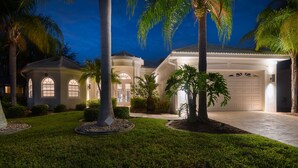 Una proprietà residenziale ben illuminata con vialetto che conduce a un garage, immersa in prati curati e palme.