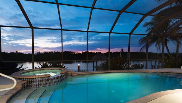 Una piscina interna con tetto in vetro, una vasca idromassaggio e vista sul tramonto su un corpo d'acqua.