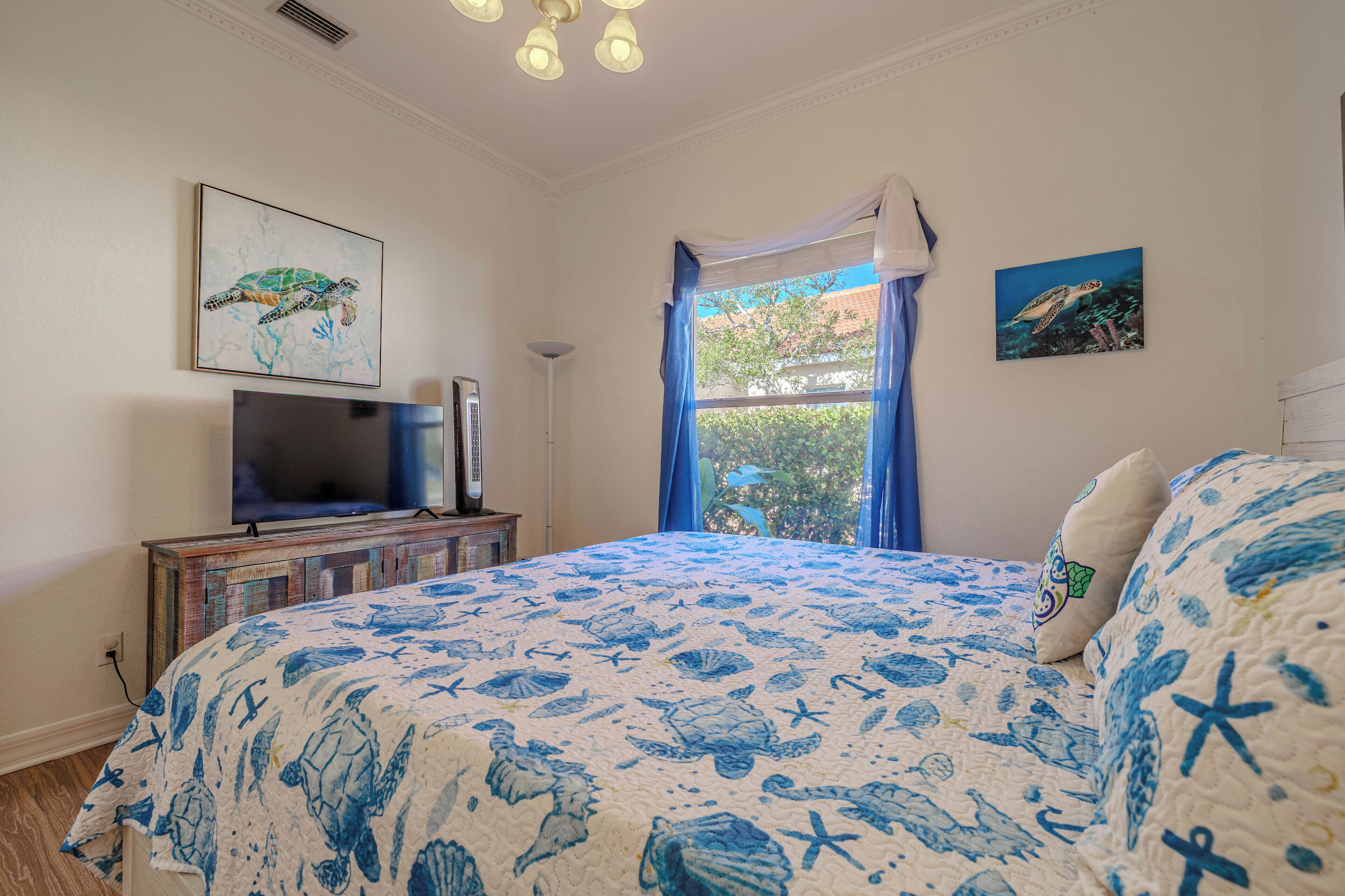 A bedroom with a bed, a TV, and artwork on the walls.