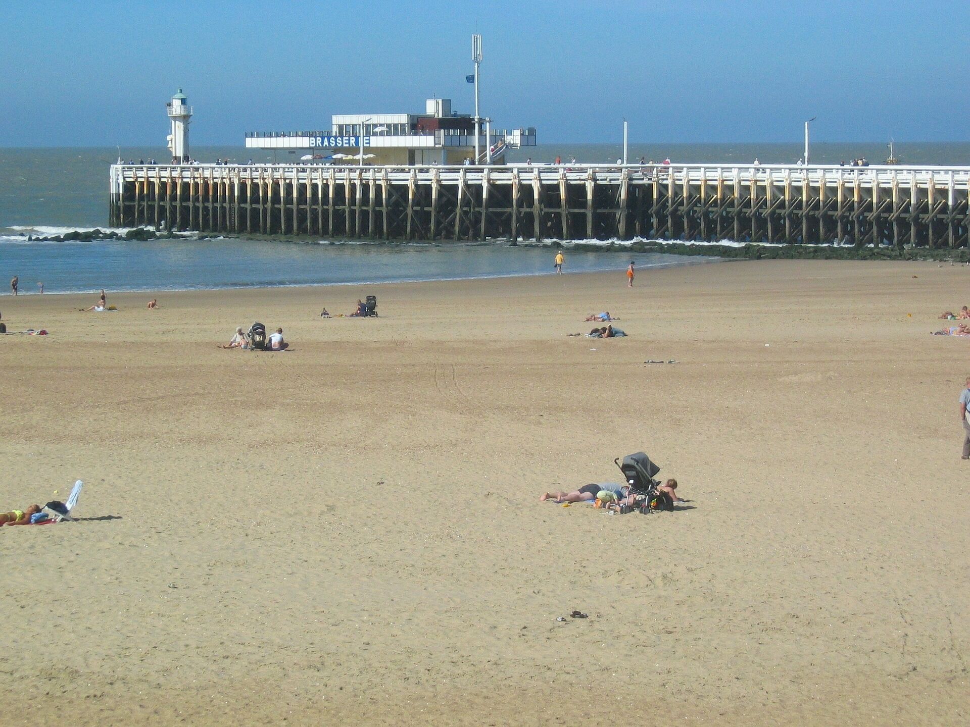 Una playa con un muelle y un faro al fondo.