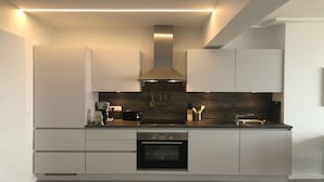 Una cocina moderna con armarios blancos, horno empotrado, cafetera y utensilios colgando.