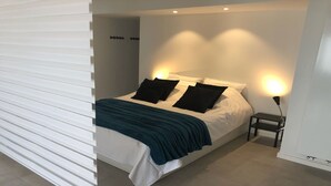 Un dormitorio moderno con una cama, almohadas, una mesita de noche y una lámpara.