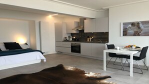 Una habitación de hotel moderna con cama, una mesa de comedor con sillas, una zona de cocina y un tapete grande.