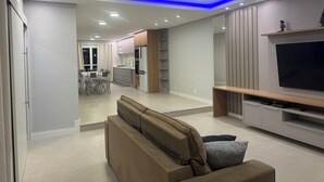 Ein modernes Wohnzimmer mit einer Couch, einem Flachbildfernseher und einer Küchenzeile mit Schränken und einem Esstisch.