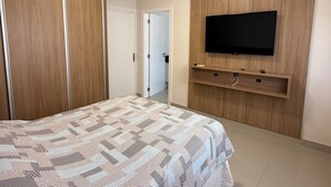 Ein Schlafzimmer mit einem Bett, einem Kleiderschrank, einem an der Wand befestigten Fernseher und einer Tür zu einem anderen Raum.