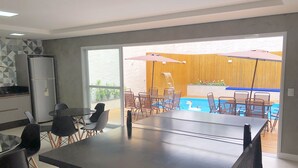 Eine moderne Küche mit Kühlschrank, ein Essbereich mit Stühlen und Tisch sowie ein Blick auf einen Poolbereich mit Sonnenschirmen.
