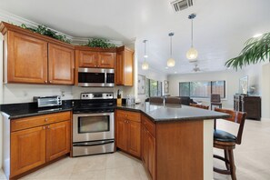 Una cocina con armarios de madera, electrodomésticos de acero inoxidable, una isla central, iluminación colgante y vistas al área de comedor.