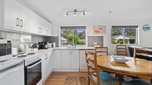 Una cocina moderna con armarios blancos, horno empotrado y una zona de comedor con mesa y sillas de madera.