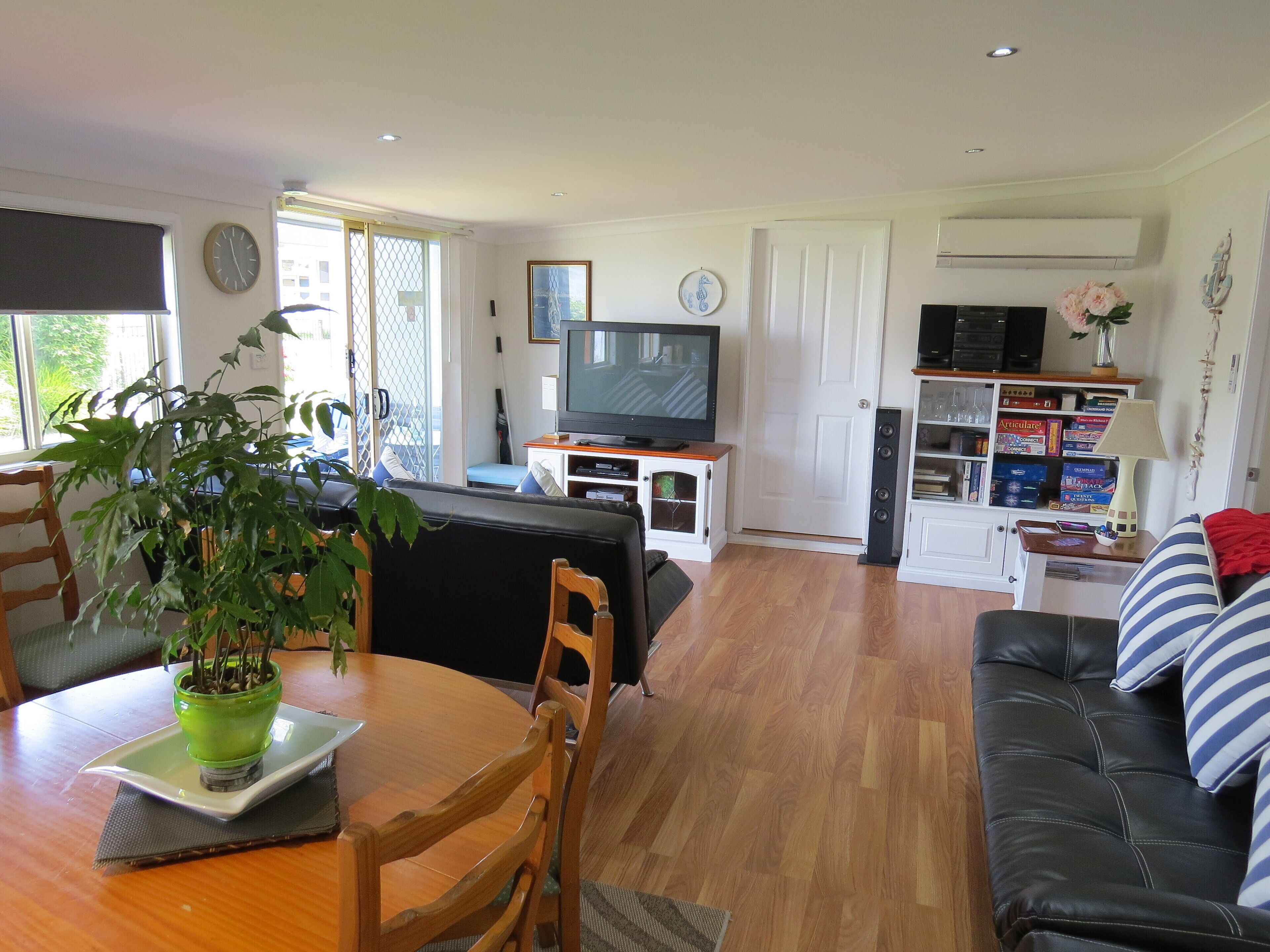 A living room with a TV, sofa, dining table, chairs, and a potted plant.