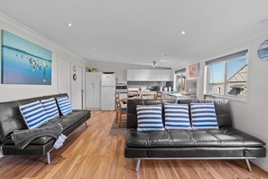 A modern living room with a black leather sofa, wooden flooring, and a large painting on the wall.