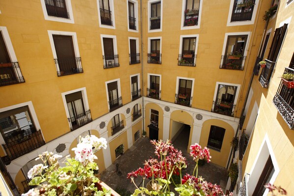 A courtyard with yellow buildings, balconies with black railings, and potted plants.