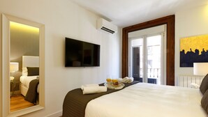 Ein Hotelzimmer mit einem großen Bett, einem an der Wand befestigten Fernseher, einem Spiegel und einem Fenster mit Blick nach draußen.