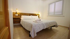 A neatly made bed with a floral bedspread, two bedside lamps, and a wooden headboard. - 112 - Apartamento Blue I (Tarifa)