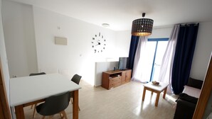 A modern living room with a dining area, a TV, and a clock on the wall. - 112 - Apartamento Blue I (Tarifa)