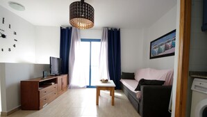 A living room with a sofa, a TV, a wooden cabinet, a table, and a washing machine. - 112 - Apartamento Blue I (Tarifa)