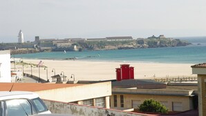 A coastal view with a beach, a lighthouse, and fortifications in the background. - 112 - Apartamento Blue I (Tarifa)