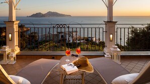 Un balcón con vistas al mar, una mesa con bebidas y un libro.