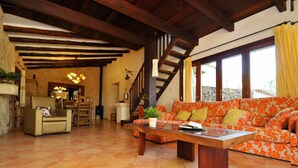 Un'ampia zona giorno con una scala in legno, un divano rivestito in tessuto floreale arancione e un'area pranzo con mobili in legno.