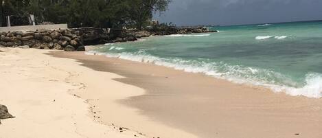 Una playa con agua turquesa cristalina, una orilla arenosa y algunos árboles al fondo.
