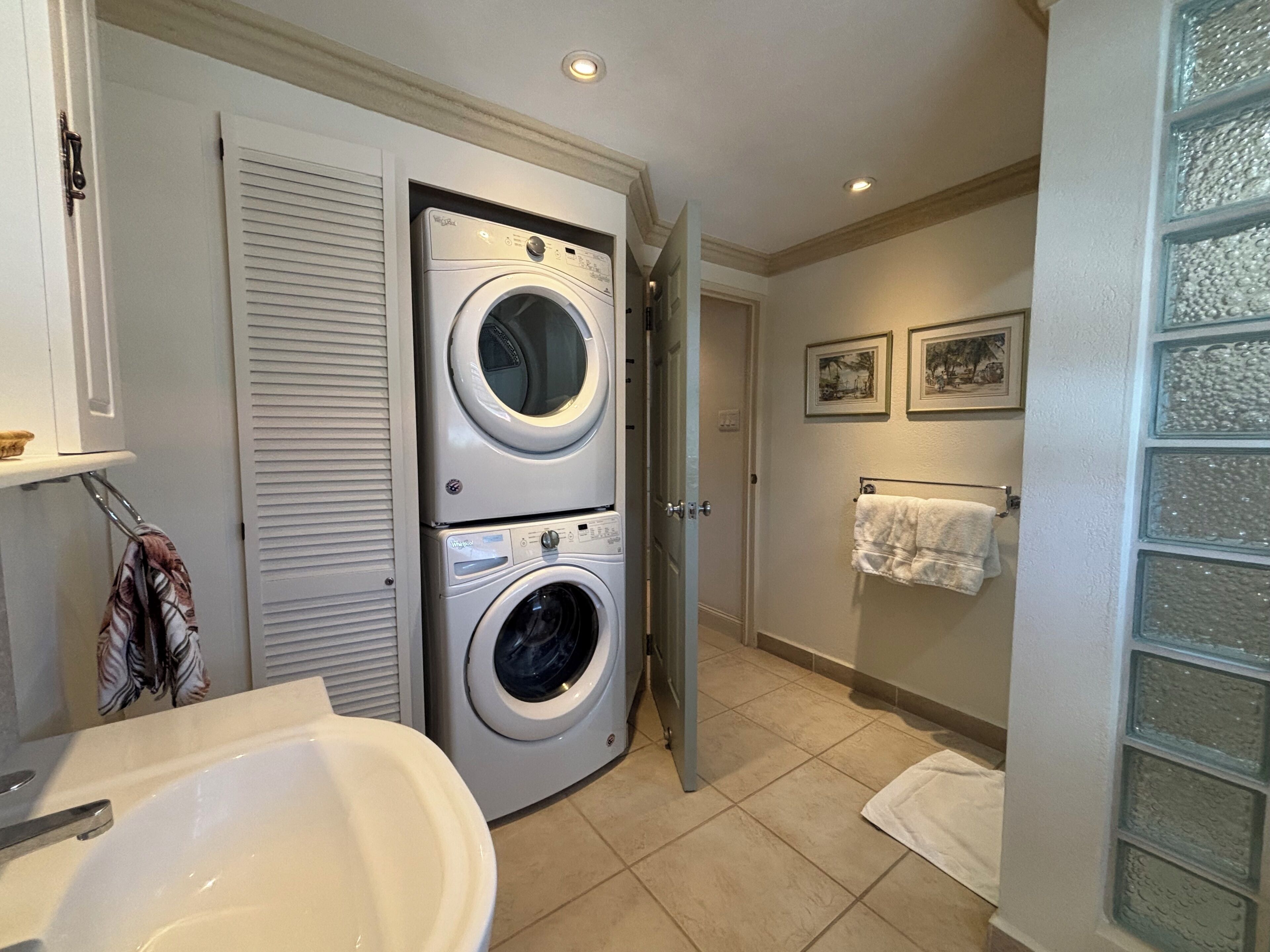 Lavandería con dos lavadoras y secadoras apiladas, un lavabo y un perchero con una toalla blanca.