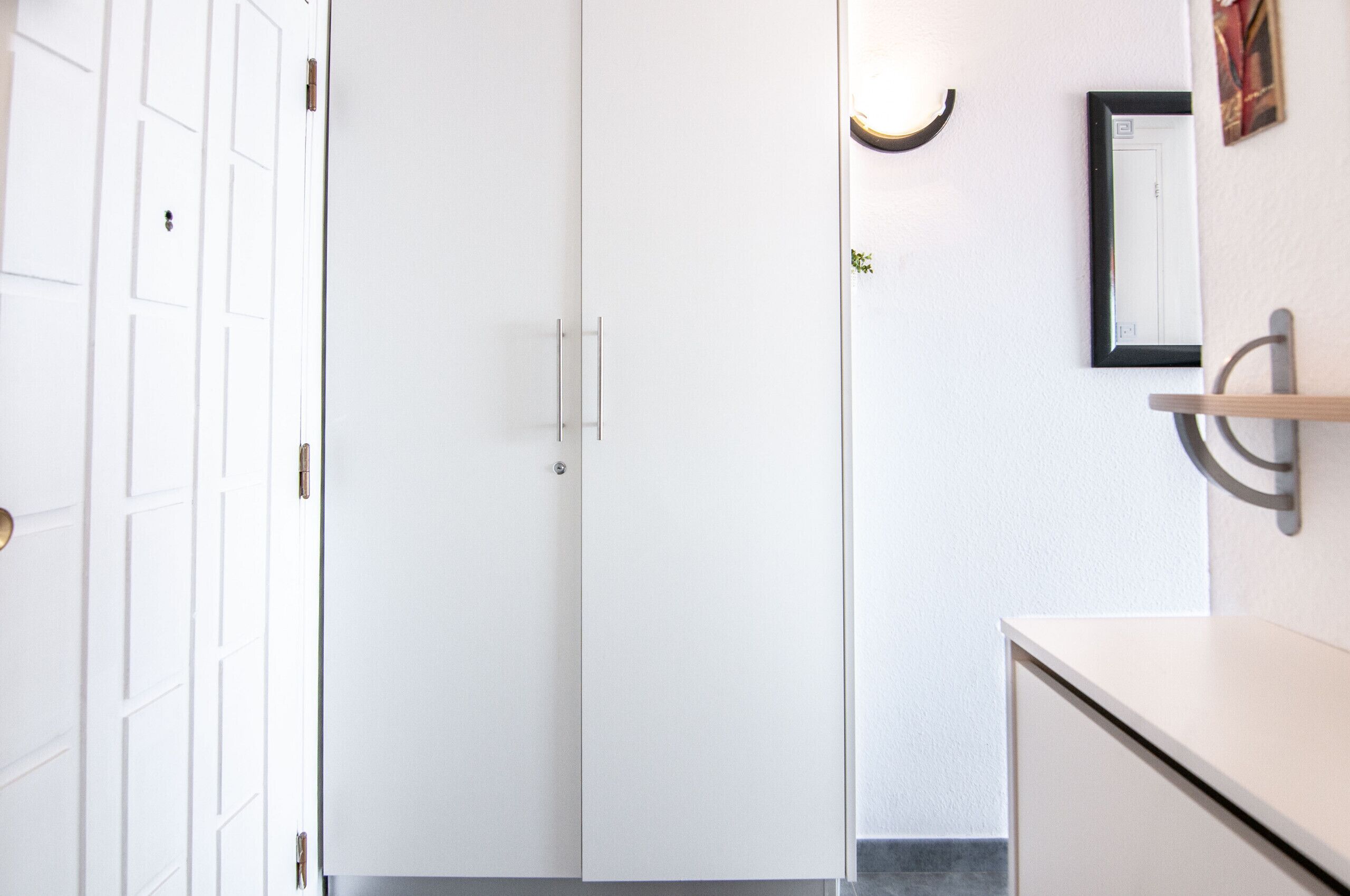 A white door with a handle, a light fixture on the wall, and a framed picture.