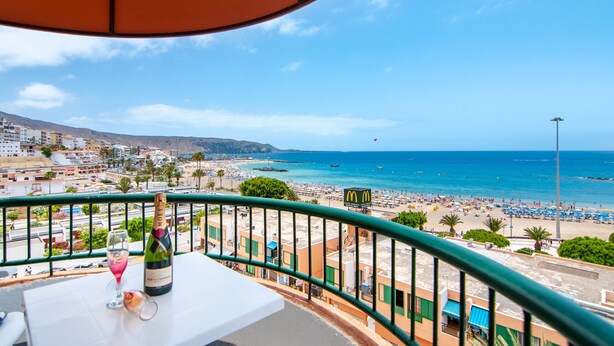 Un balcon donnant sur une plage, une enseigne de McDonald's et une bouteille de champagne posée sur une table.