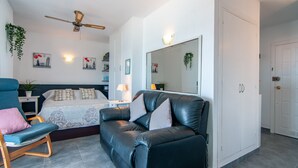 Une chambre à coucher moderne avec un lit, un canapé en cuir noir, un fauteuil bleu, un ventilateur de plafond et un grand miroir.