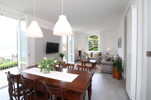 A spacious living area with a wooden dining table, chairs, a sofa, and a TV mounted on the wall. - Lake cottage Bellagio, a beautiful dehors with wonderful view on the lake (Bellagio)