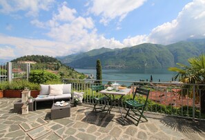 A terrace with stone flooring, a sofa, two chairs, a table, and a view of a lake and mountains. - Lake cottage Bellagio, a beautiful dehors with wonderful view on the lake (Bellagio)