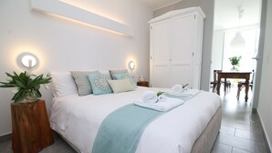 Ein ordentlich bezogenes Bett mit einer türkisfarbenen Tagesdecke und weißen Bettwäsche, ein Nachttisch aus Holz mit einer Pflanze und ein weißer Kleiderschrank.