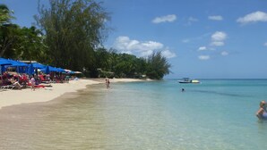 Una playa con agua turquesa cristalina, sombrillas y gente relajándose.