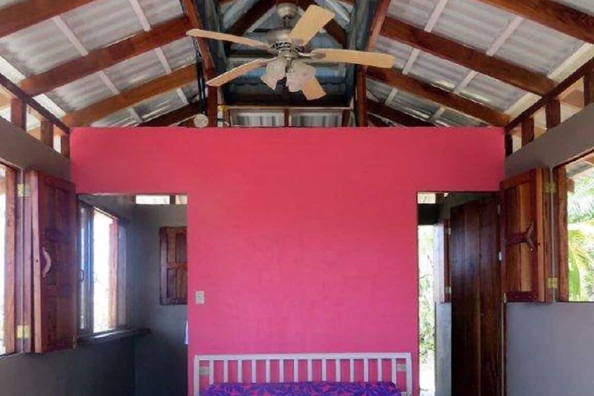 A bedroom with a bed, a ceiling fan, and a red wall.