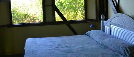 A bed with a floral bedspread in a room with a window overlooking greenery.