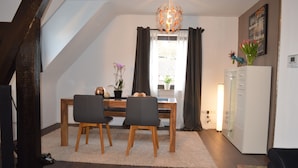 Een eetruimte met een tafel, stoelen, een kroonluchter, een potplant en een koelkast.
