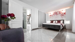 A modern bedroom with a bed, a chair, a vase with flowers, and a hallway leading to a bathroom.