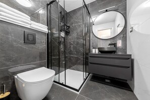 A modern bathroom with a glass shower enclosure, a toilet, a vanity with a sink, and a large mirror.