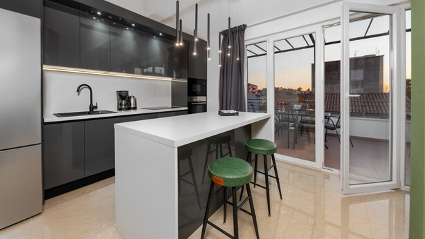 A modern kitchen with a central island, bar stools, and a view through large sliding doors to an outdoor area.