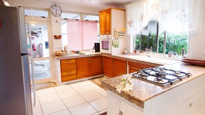 A kitchen with wooden cabinets, a gas stove, a refrigerator, and a window with curtains. - Pension Farehau (Faaa)