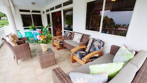 A covered patio area with wicker furniture, a table with a potted plant, and a view of the outdoors. - Pension Farehau (Faaa)