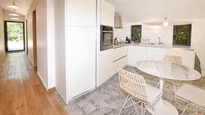 A modern kitchen with white cabinetry, a built-in oven, and a dining area with a round table and wicker chairs. - Luxurious home in Malaucene (Malaucene)