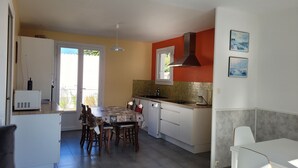 Una cocina con mesa de comedor, sillas, cafetera y ventana.