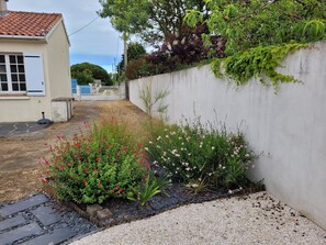 Un jardín residencial con un sendero pavimentado, plantas en flor y una pared blanca.