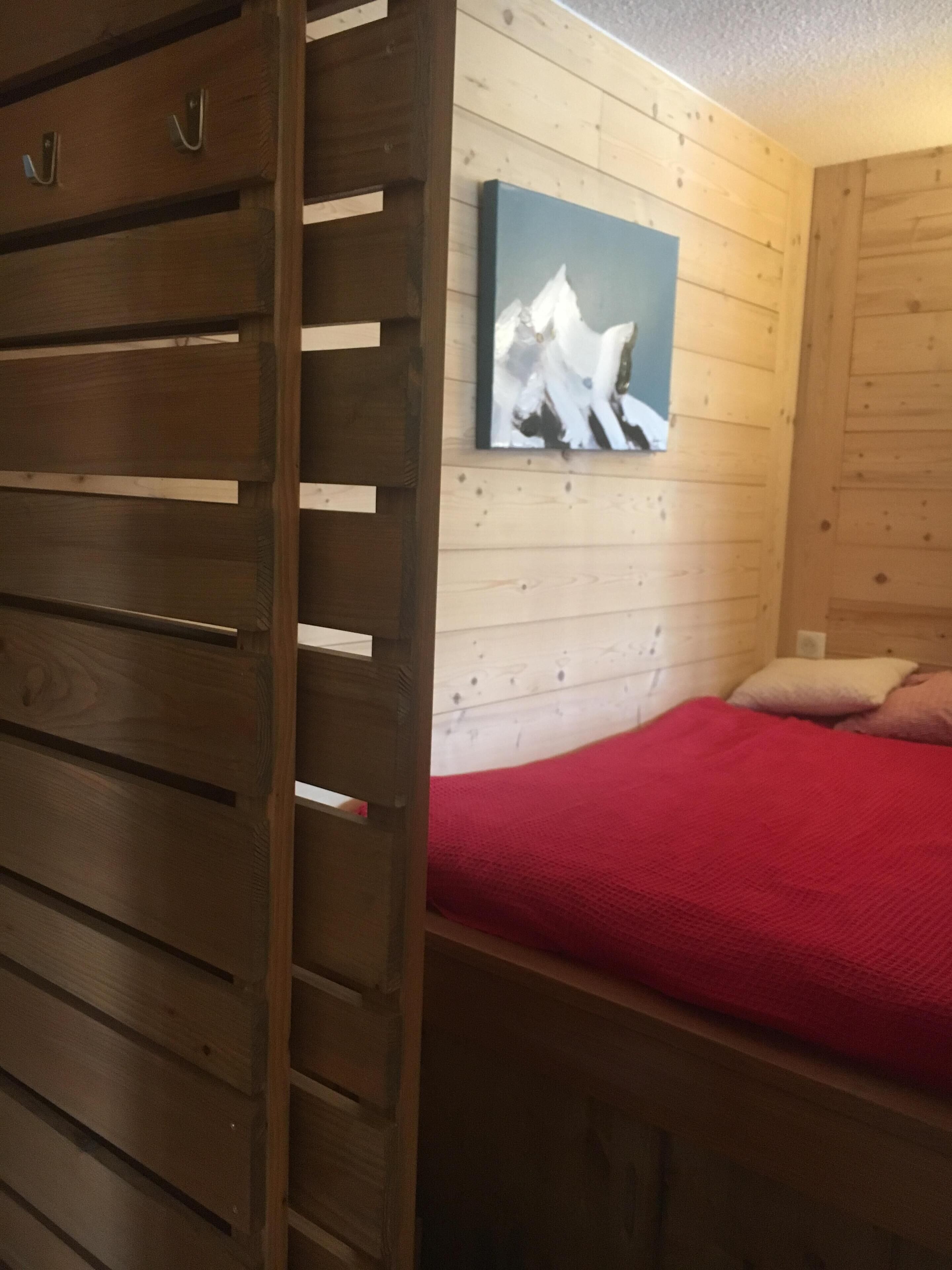 Una habitación de madera con una cama, un edredón rojo y un cuadro en la pared.