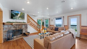 A spacious living room with a stone fireplace, a wooden staircase, a large sofa, and a television mounted on the wall. - Trails End Cabin with a hot tub, fire pit, & indoor pool! (Bryant)
