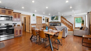 A spacious kitchen with wooden cabinets, a dining area with a table and chairs, and a cozy living room with a sofa and a staircase. - Trails End Cabin with a hot tub, fire pit, & indoor pool! (Bryant)