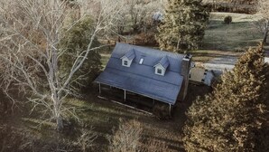 Ein Haus mit Metallbedachung, zwei kleine Anbauten und ein großer Baum im Vordergrund.