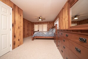 A bedroom with wooden walls, a bed with patterned bedding, a dresser, and a ceiling fan. - Experience Pisgah Forest charm near Dupont State and Pisgah National Forests (Pisgah Forest)