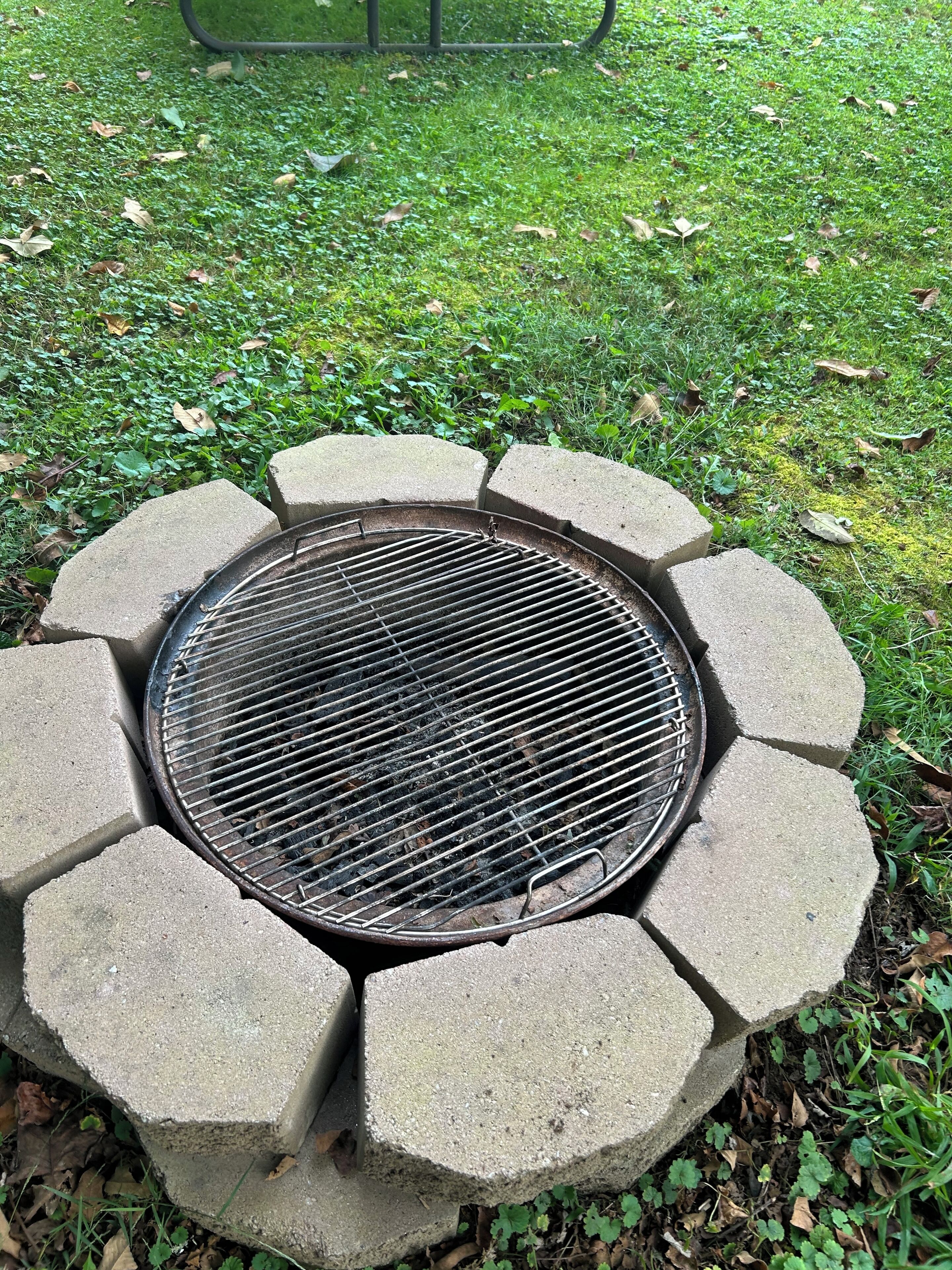 A circular outdoor grill with a metal grate, surrounded by concrete blocks.