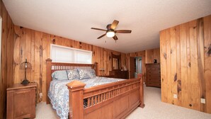 Ein Schlafzimmer mit einem hölzernen Bett, Deckenventilator, Nachttisch, Schminktisch und einem Fenster mit Jalousien.